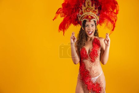Téléchargez les photos : Portrait de femme afro brésilienne en tenue de carnaval avec les doigts croisés souhaitant bonne chance. Femme danseuse de carnaval croise les doigts en attendant le résultat du placement de l'école de samba - en image libre de droit