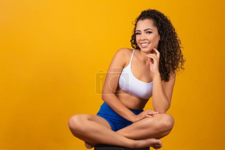 Téléchargez les photos : Belle jeune femme afro en tenue de fitness souriante regardant la caméra avec de l'espace pour le texte. Horizontal - en image libre de droit