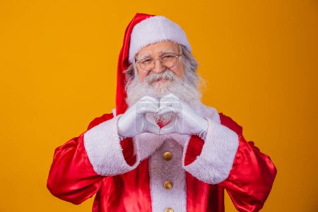 Téléchargez les photos : Père Noël faisant signe de coeur avec ses mains et fond jaune - en image libre de droit