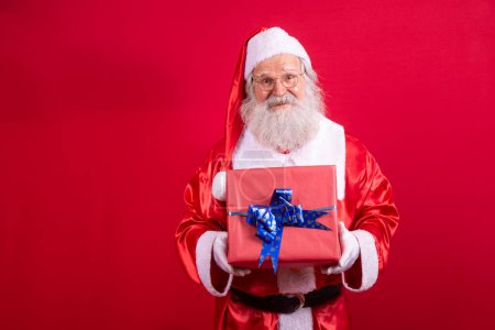Photo for Santa Claus holding a Christmas present on red background. - Royalty Free Image