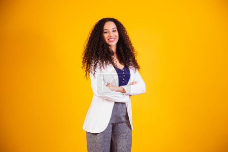 Foto de Joven mujer de negocios afro con los brazos cruzados sobre fondo amarillo. - Imagen libre de derechos