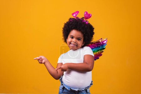 Téléchargez les photos : Adorable afro girl habillée en tenue colorée sur fond jaune. Journée de l'enfant. afro fille avec costume - en image libre de droit