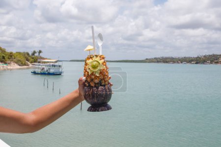 Téléchargez les photos : Mains tenant boisson à l'ananas avec fond de plage. - en image libre de droit