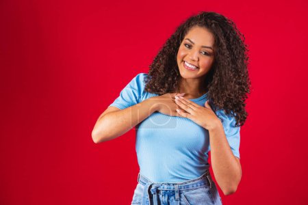 Photo for Grateful hopeful happy black woman holding hands on chest feeling pleased thankful, sincere african lady expressing heartfelt love appreciation gratitude honesty isolated on red studio background - Royalty Free Image