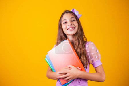 Photo for Beautiful smiling girl holding books going to school. close up portrait, isolated yellow background, childhood. child hugging notebooks. lifestyle, interest, hobby, free time, free time - Royalty Free Image