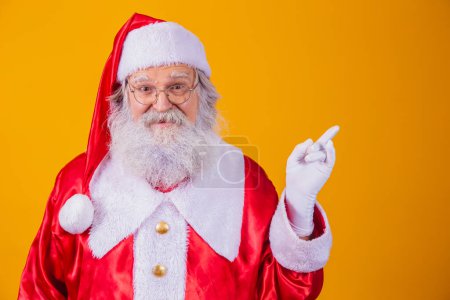 Photo for Funny happy excited old bearded Santa Claus face wearing costume looking at camera showing pointing fingers aside advertising Christmas promotion, New Year xmas discount ad isolated on yellow - Royalty Free Image
