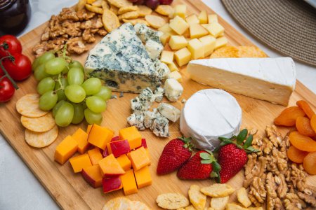Foto de Plato de queso con variedad de aperitivos en la mesa. Platos de fresa, albaricoque, uva y queso de grano sobre la mesa - Imagen libre de derechos