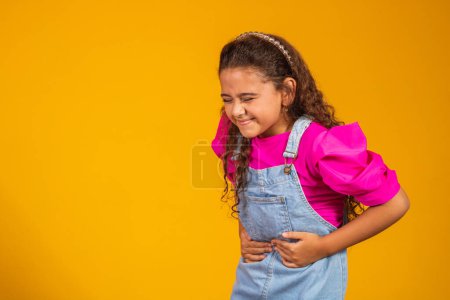 Foto de Una chica sobre un fondo amarillo tiene dolor de estómago. Tomando de la mano el vientre y el sufrimiento. - Imagen libre de derechos