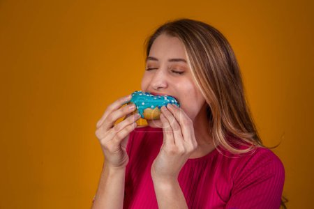 Téléchargez les photos : Portrait d'une jeune fille blonde mangeant un délicieux beignets colorés. - en image libre de droit