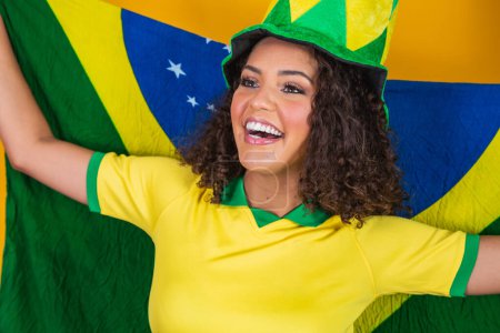 Téléchargez les photos : Afro fille acclamant pour l'équipe brésilienne préférée, tenant drapeau national en arrière-plan jaune
. - en image libre de droit