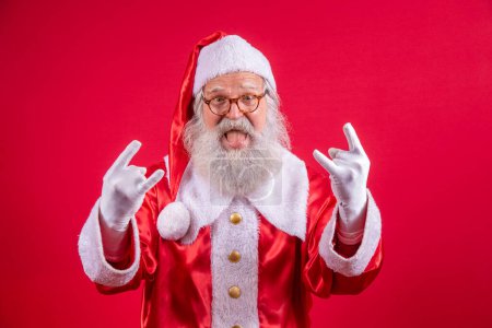 Téléchargez les photos : Père Noël faisant signe rock n roll avec les mains et le fond rouge. - en image libre de droit