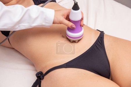 Photo for Cropped shot of a professional dermatologist performing radiofrequency lifting procedure on the stomach of a woman. Female client getting rf-lifting treatment on her belly at cosmetology clinic - Royalty Free Image