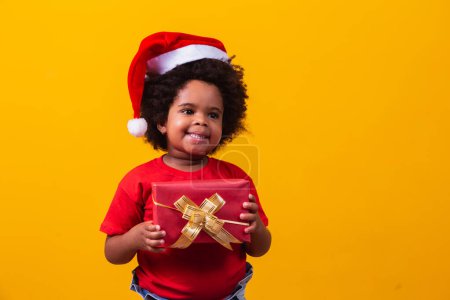 Photo for Smiling afro child in Santa Claus red hat holding christmas gift in hand. Christmas concept. - Royalty Free Image