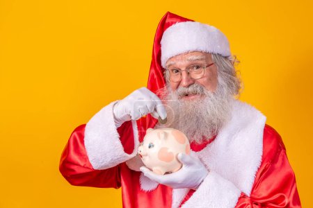 Photo for Santa Claus putting coin into a ceramic piggy bank. Savings concept for the end of the year. Spending over Christmas. Spent on Christmas presents. - Royalty Free Image