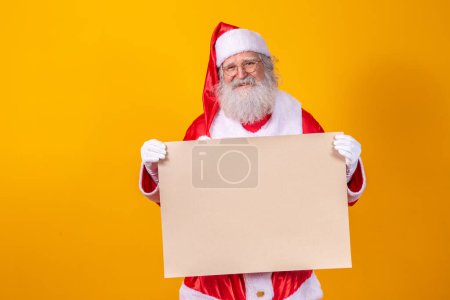 Foto de Feliz Santa Claus sosteniendo un tablero en blanco aislado sobre fondo amarillo con espacio de copia. - Imagen libre de derechos