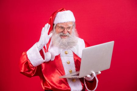 Foto de Santa Claus usando un portátil sobre fondo rojo. - Imagen libre de derechos