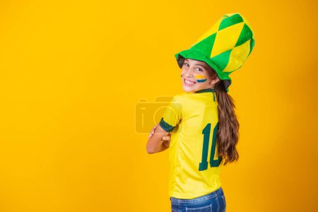 Téléchargez les photos : Petite fille fan brésilienne avec son dos sur fond jaune avec chemise brésilienne - en image libre de droit