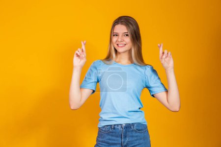 Téléchargez les photos : Image d'une jeune fille heureuse positive isolée sur fond de mur jaune faire un geste plein d'espoir s'il vous plaît. Jolie fille avec ses doigts croisant sur fond jaune. - en image libre de droit