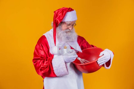 Téléchargez les photos : Père Noël avec un bol battant gâteau sur fond jaune - en image libre de droit