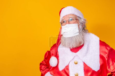 Téléchargez les photos : Vrai Père Noël avec un fond jaune, portant un masque de protection, des lunettes et un chapeau. Noël avec distance sociale. Covid-19 - en image libre de droit