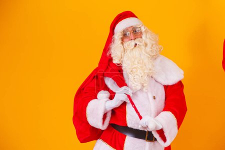 Téléchargez les photos : Père Noël avec un énorme sac dans la hâte de livrer des cadeaux de Noël. Père Noël sur fond jaune - en image libre de droit