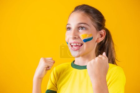 Photo for Beautiful little girl rooting for her team on yellow background. Little girl celebrating the goal and celebrating Brazil's victory - Royalty Free Image