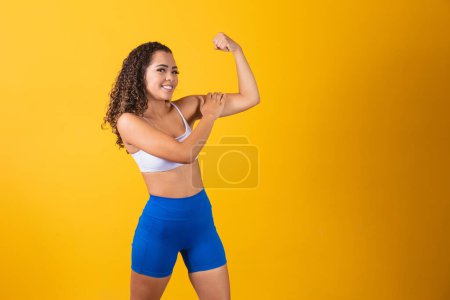 Téléchargez les photos : Image d'une fille afro-américaine forte et confiante, fléchissant ses biceps et le pointant du doigt. - en image libre de droit