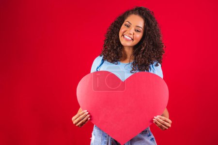 Photo for Afro girl holding in hands heart shape amour isolated over red background - Royalty Free Image