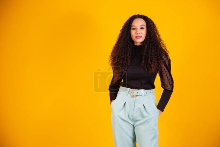 Photo for Beauty portrait of a Brazilian woman with afro hairstyle and glamour makeup. Latin woman. Mixed race. Curly hair. Hair style. Yellow background - Royalty Free Image