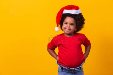 Téléchargez les photos : Petite fille afro en t-shirt rouge et chapeau de Père Noël habillé pour Noël. Campagne de Noël et Nouvel An - en image libre de droit