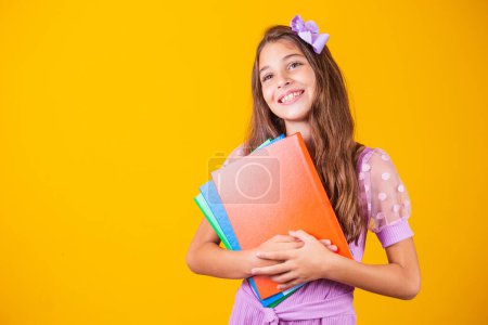 Photo for Beautiful smiling girl holding books going to school. close up portrait, isolated yellow background, childhood. child hugging notebooks. lifestyle, interest, hobby, free time, free time - Royalty Free Image