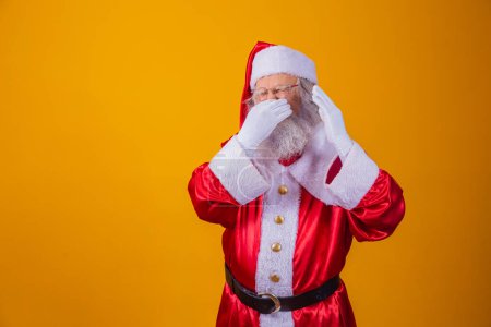 Téléchargez les photos : Le Père Noël isolé sur fond jaune, sentant quelque chose de puant et dégoûtant, une odeur insupportable, retenant son souffle avec les doigts dans le nez. Concept de mauvaises odeurs. - en image libre de droit