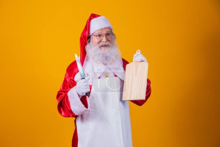Téléchargez les photos : Père Noël habillé en tablier tenant une assiette de viande vide et un couteau - en image libre de droit