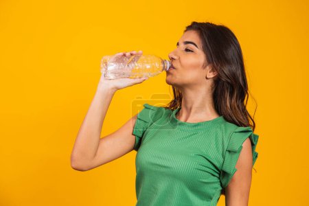 Photo for Young woman drinking water from a small bottle on yellow background with free space for text. Young man drinks water and hydrates - Royalty Free Image