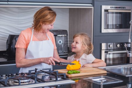 Photo for Elderly mother and little daughter cooking together. Mother and daughter cutting vegetables for cooking - Royalty Free Image