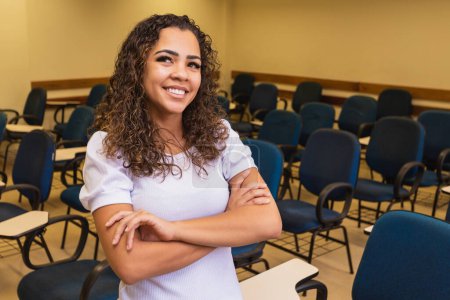 Photo for Afro student in classroom with arms crossed looking at camera smiling. Young student with the classroom in the background. - Royalty Free Image