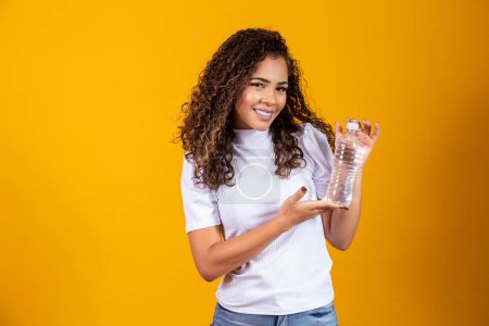 Foto de Mujer sosteniendo una botella de agua sobre fondo amarillo. Beber agua! - Imagen libre de derechos