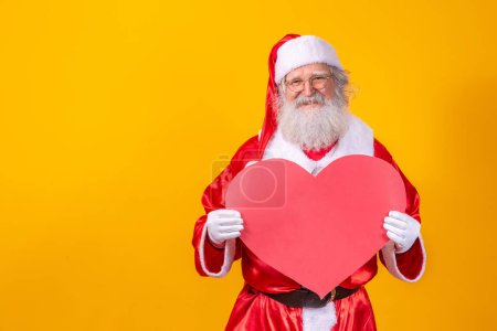 Photo for Santa Claus holding big red heart card in yellow background. Romantic Santa Claus. - Royalty Free Image