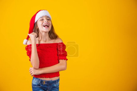 Foto de Niña vestida para Navidad señalando con el pulgar el espacio libre para el texto. Promoción y campañas de fin de año - Imagen libre de derechos