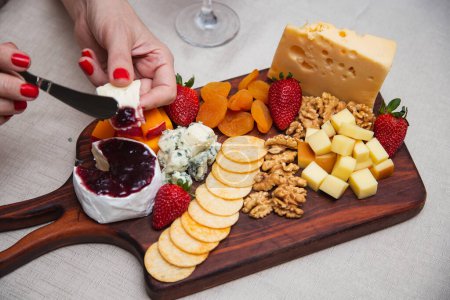Téléchargez les photos : Mains passant la gelée sur le fromage avec divers fromages sur la plaque de fond. - en image libre de droit