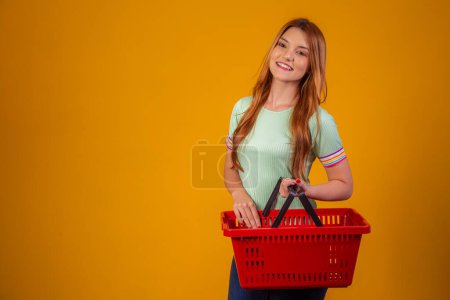 Photo for Smiling redhair woman holding empty shopping basket looking at camera smiling - Royalty Free Image