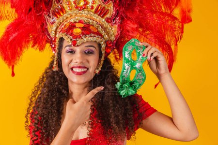 Foto de Joven afro mujer en traje de samba y carnaval sosteniendo una máscara verde sonriendo a la cámara. - Imagen libre de derechos
