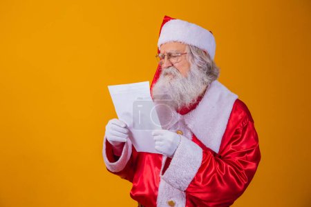 Téléchargez les photos : Joyeux Père Noël tenant du papier vintage sur fond jaune. Joyeux Noël et Nouvel An concept. Espace de copie. Difficulté à lire. Une écriture affreuse.
. - en image libre de droit