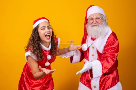 Foto de Feliz Navidad. Noelete joven y Santa Claus real interactuando jugando sobre fondo amarillo - Imagen libre de derechos