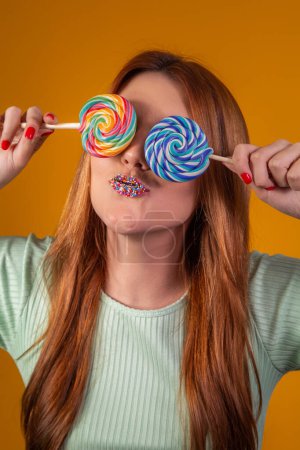 Photo for Young red-haired woman with colorful lollipops blindfolding her eyes. fashion concept - Royalty Free Image