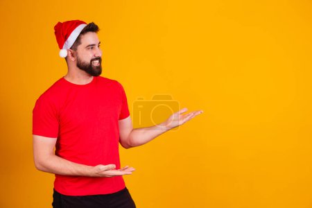 Photo for Handsome man dressed for christmas wearing santa claus hat pointing to free text space. year-end promotion - Royalty Free Image
