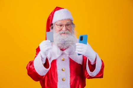 Photo for Portrait of nice handsome amazed stunned bearded Santa holding in hand plastic card device web app shop buy order delivery pay wireless payment isolated on yellow background - Royalty Free Image