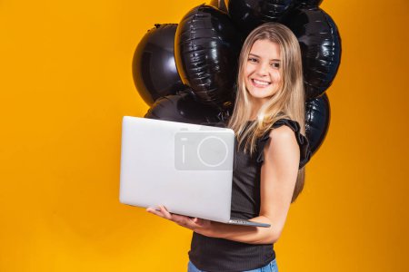 Photo for Smiling cheerful funny young brunette woman 20s  using laptop pc computer on bright yellow colour background with air balloons studio portrait. Black friday sale - Royalty Free Image