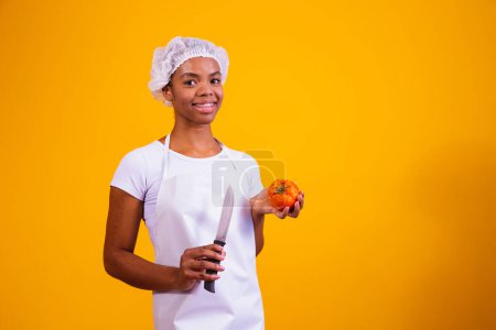 Mujer en delantal sosteniendo un cuchillo y un tomate.
