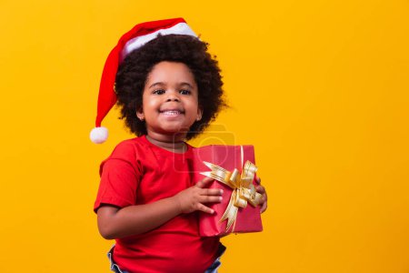 Photo for Smiling afro child in Santa Claus red hat holding christmas gift in hand. Christmas concept. - Royalty Free Image